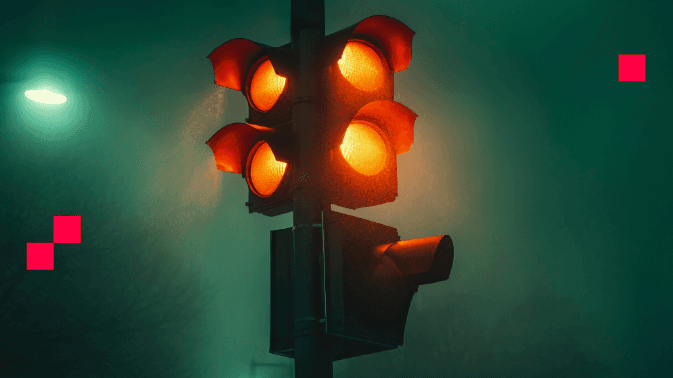 Un semáforo vertical en la noche, con todas sus luces encendidas en amarillo y naranja, creando un efecto visual intenso y poco común —ya que normalmente solo una luz está activa. El fondo es oscuro y neblinoso, con una luz verde difusa en el extremo izquierdo que contrasta con el tono cálido del semáforo. La escena transmite una sensación de caos, advertencia o anomalía, ideal para simbolizar decisiones complejas, sistemas fuera de control o momentos de incertidumbre.